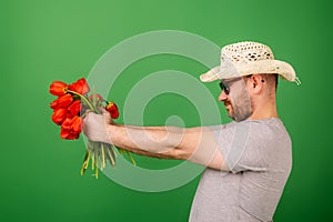 A man in a hat and sunglasses shows holding out a bouquet of tulip flowers on a green background. Romanticism, give, apologize