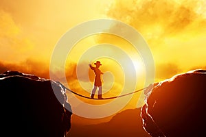 Man in hat walking, balancing on rope over mountains