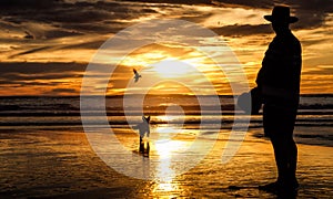 Man with hat walking a dog on Piha Beach