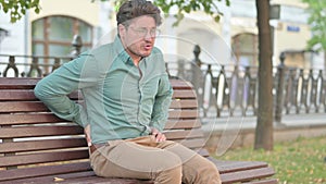 Man having Back Pain while Sitting on Bench