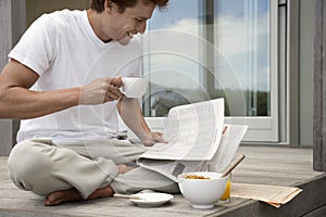Man Having Breakfast And Reading Newspaper On Porch