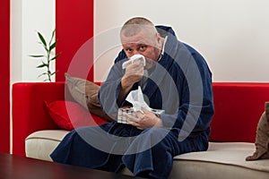 Man having a cold holding tissue with box full of tissues