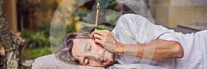 Man having an ear candle therapy against the backdrop of a tropical garden BANNER, LONG FORMAT