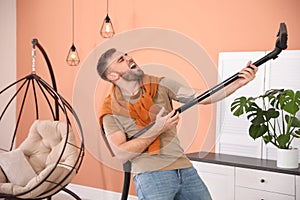 Young man having fun while vacuuming at home