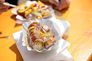 Man having German Currywurst sausage with curry sauce, French fries and mayonnaise on food market