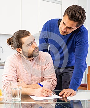Man having problems with some documents, worriedly discussing with friend at home table