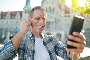 Man having video call talking via smartphone and internet putting earphones while visiting new city.