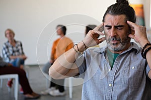 Man with head in hand sitting on chair while friends discussing in background