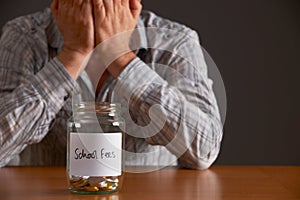 Man With Head In Hands Looking At Jar Labelled School Fees photo