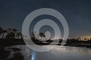 A man with a headlamp on a lookout tower on the Seli swamp in winter at night with a starry sky