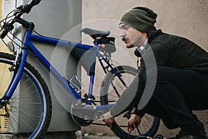 Man with headphones checking bicycle tire outdoors in urban setting