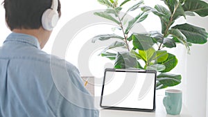 Man with headphones and digital tablet with blak screen on working table background for mock up, template