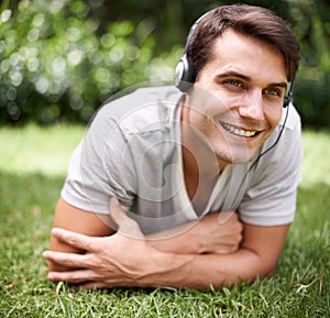 Man, headphones and grass with smile, relax and music in park or garden. Student, rest and audio for podcast, wellness