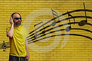 Man with headphones listening to music standing in front of a yellow brick wall