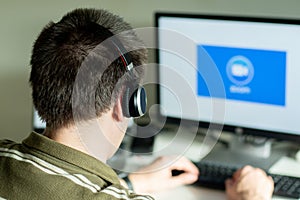 Man with headphones looking on the monitor with zoom cloud meetings logo. Coronavirus lockdoown