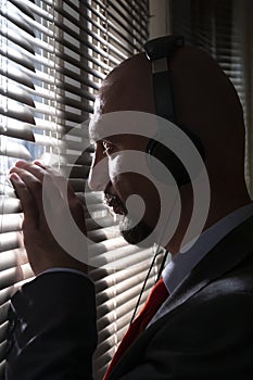 A man with headphones looks through the blinds of the window, eavesdrops on a conversation, spies on people.Concept: a special age