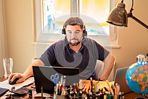 Man with headphones and microphone having conference call online sitting at home office with two laptops.