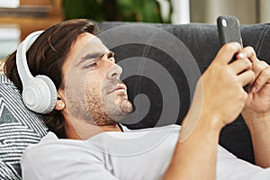 Man, headphones and phone for music on couch, relax and listen to song and scroll on social media. Male person, home and