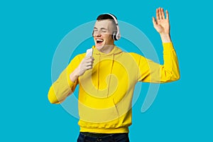 Man In Headphones Singing Holding Phone Like Microphone, Blue Background