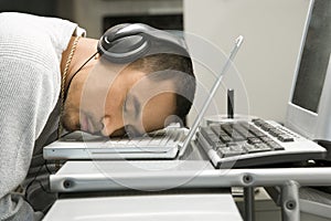 Man with headphones sleeping on laptop.