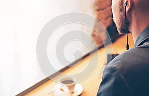 The man in headphones using mobile phone, sitting with coffee at cafe