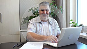 A man with a headset works at home on a computer, then turns and smiles at the camera.