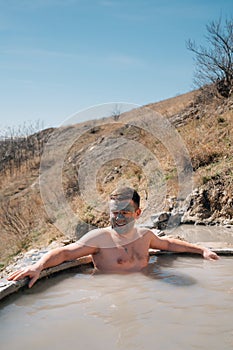 a man with healing clay on the face bathes in a hydrogen sulfide thermal spring.