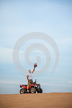 Man with helmet in hand poses on atv in desert