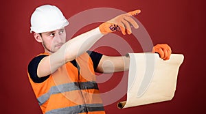 Man in helmet, hard hat holds building plan, controls works, red background. Foreman concept. Engineer, architect