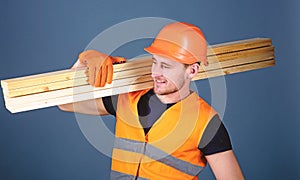 Man in helmet, hard hat and protective gloves holds wooden beam, grey background. Carpenter, woodworker, labourer
