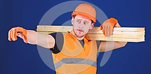 Man in helmet, hard hat and protective gloves pointing direction, blue background. Wooden materials concept. Carpenter