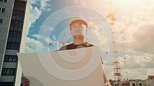 A man in a helmet is holding a construction plan in his hands. A builder is checking blueprints.