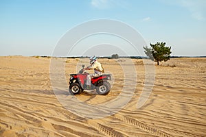 Man in helmet rides on atv in desert sands