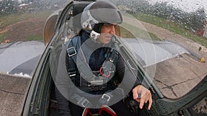 A man in helmet student in a flight school for the first time sits in gray real plane. Pilot shows different gestures. Inside view