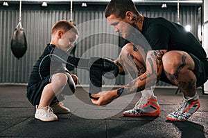 Man is helping child to wear the glowes. Coach is teaching the boy box techniques indoors