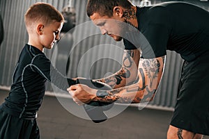 Man is helping child to wear the glowes. Coach is teaching the boy box techniques indoors