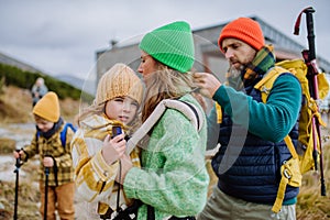 Man helping his wife with their little tired daughter, giving her into child carrier, during autumn hike in mountains.