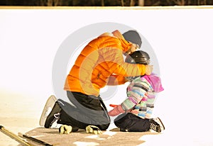 A man helping a little girl put on a hockey helmet on an outdoor rink