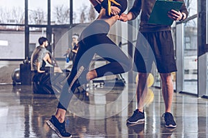 Man helping sportive woman exercising with trx gym equipment