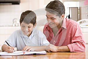 Man helping young boy in kitchen doing homework an
