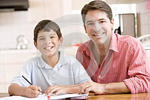 Man helping young boy in kitchen doing homework an