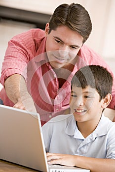 Man helping young boy in kitchen with laptop