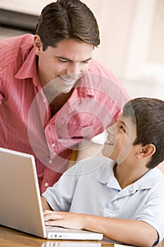 Man helping young boy in kitchen with laptop