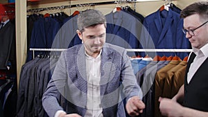 Man helps another try on a suit in a clothing store