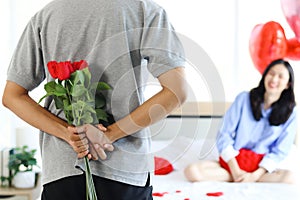 Man hiding beautiful red rose bouquet behind back, ready to give Valentine flower present to lover girlfriend for celebration,