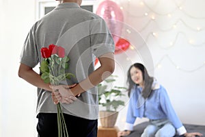 Man hiding beautiful red rose bouquet behind back, ready to give Valentine flower present to lover girlfriend for celebration,