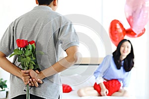 Man hiding beautiful red rose bouquet behind back, ready to give Valentine flower present to lover girlfriend for celebration,