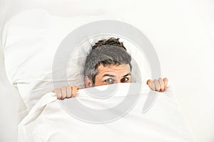 Man with hiding in bed under blanket at home.