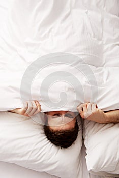 Man hiding in bed under sheets.