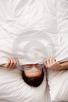 Man hiding in bed under sheets.